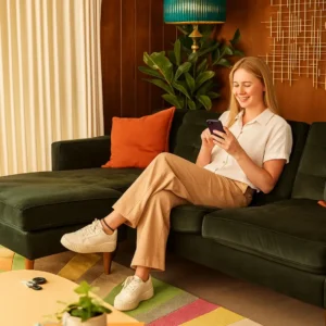 Young woman sitting on a sofa using a smartphone app to control her smart home security system, highlighting wireless alarm features and remote monitoring convenience.